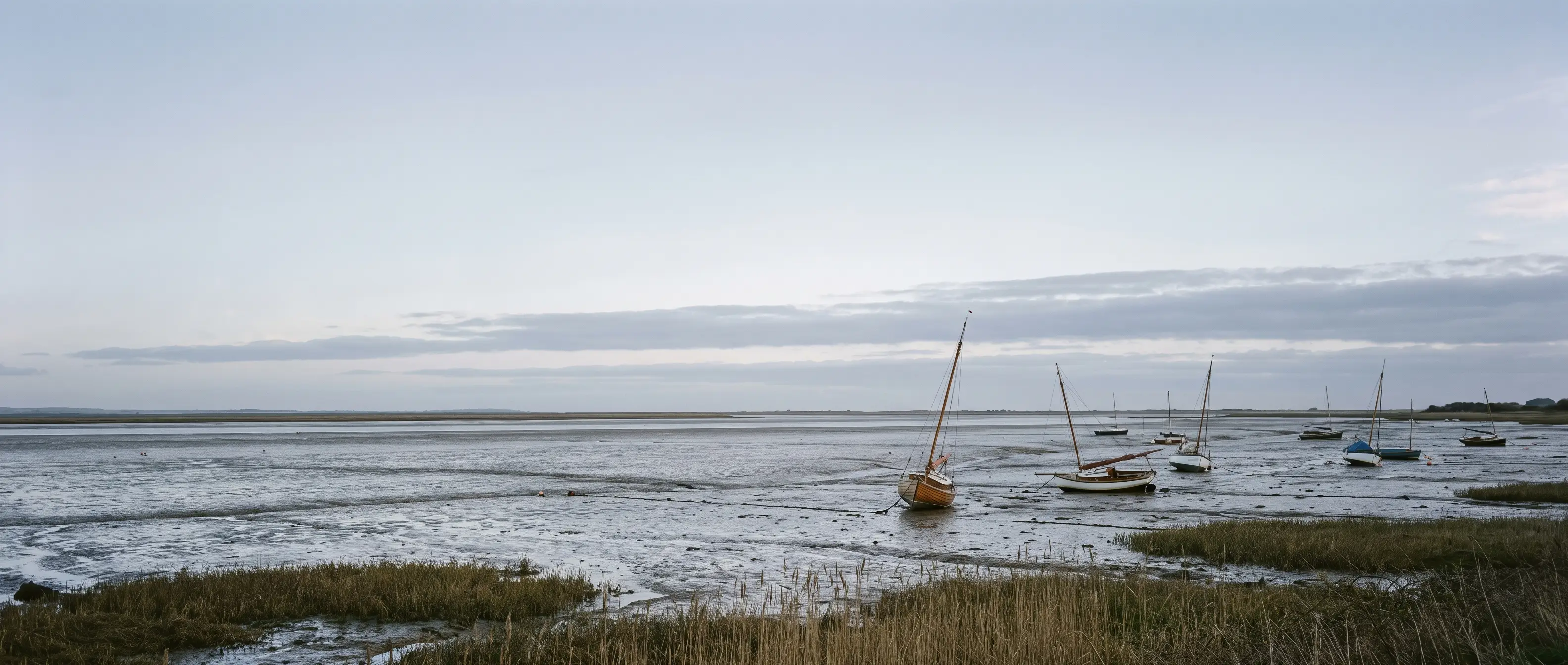 The Deben at low water, boats leaning on the mud, reeds and a wide grey Suffolk sky