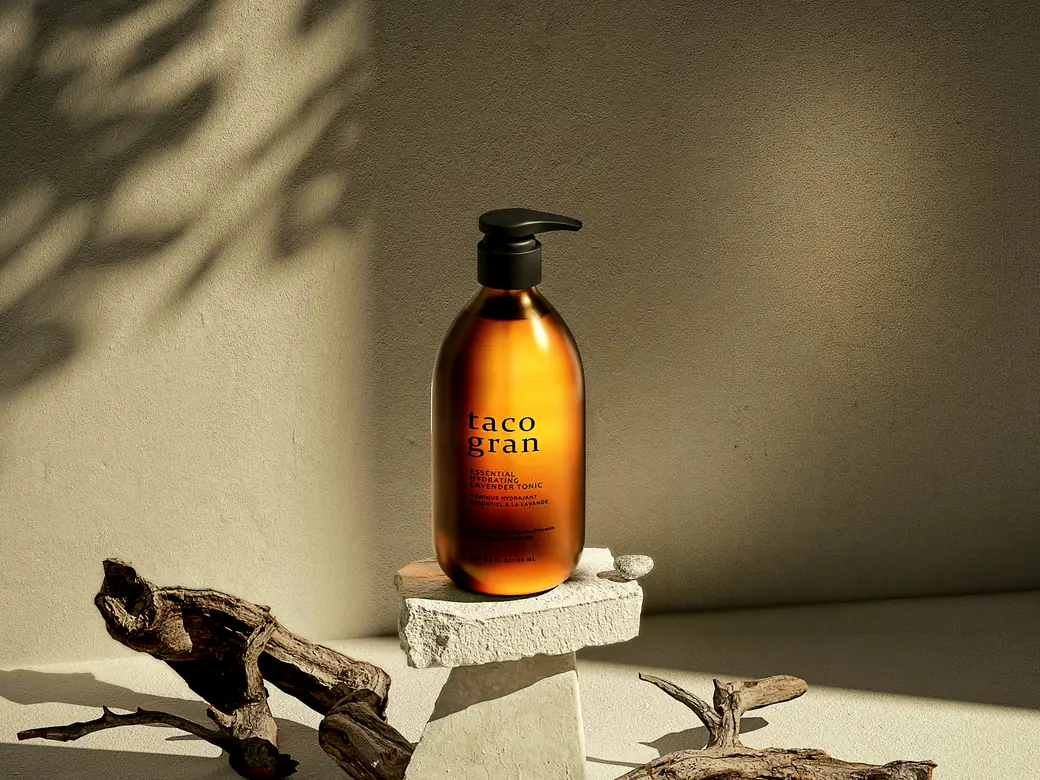 A retouched product shot of an amber Taco Gran tonic bottle on stone plinths, with driftwood and palm shadows